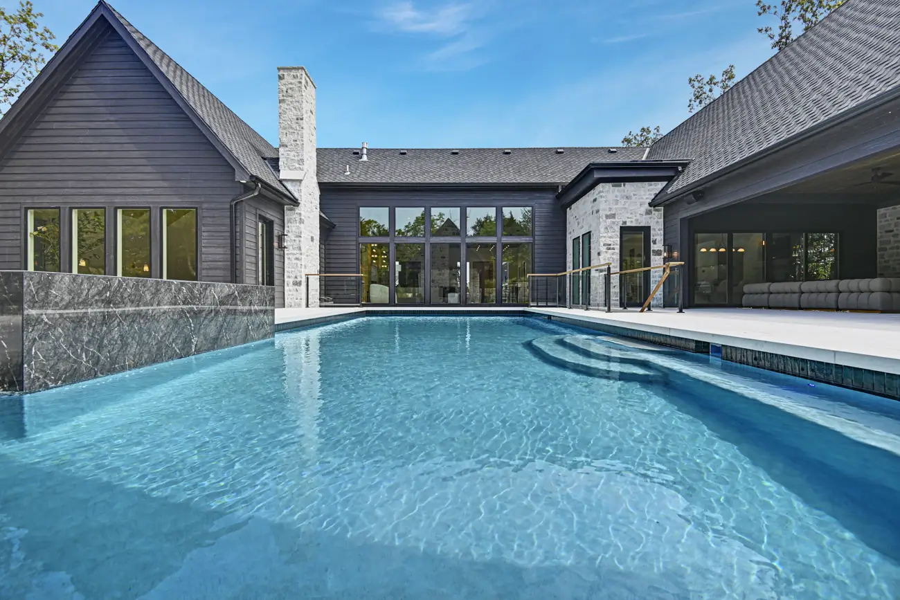 Pool with marble spillover wall beside a dark timber home